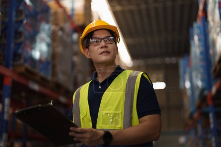 Téléchargez les photos : Portrait de l'homme asiatique superviseur d'entrepôt travail entrepôt de distribution à et la gestion des stocks et de la logistique. Inspecteur industriel travaillant en usine. - en image libre de droit