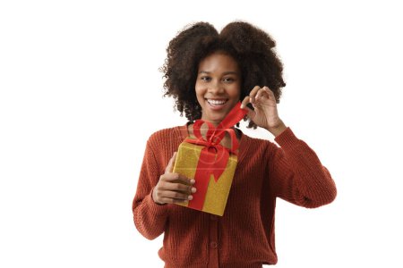 Photo for Cute african-american young woman in red knitted sweater holding gift box on white wall background. Girl smiling, she is happy to get present for Christmas festival and happy new year's. - Royalty Free Image