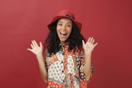 Téléchargez les photos : Portrait femme brésilienne portant un chapeau rouge et des vêtements de style décontracté sur fond rouge. - en image libre de droit
