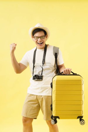 Téléchargez les photos : Un jeune voyageur asiatique joyeux portant un chapeau debout tout en tenant une carte et un sac de voyage avec des bagages. Vacances d'été et aventure concept de voyage. - en image libre de droit