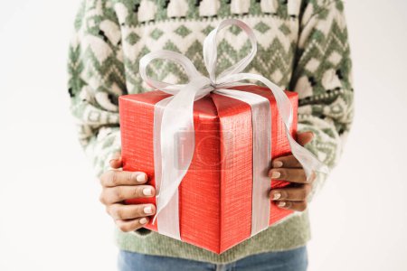 Téléchargez les photos : Personnes en pull tricoté donne une boîte cadeau à l'appareil photo sur fond blanc mur. Fête de Noël et bonne année. - en image libre de droit