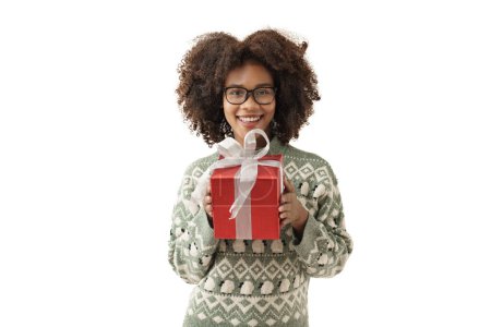 Foto de Linda mujer joven afroamericana en jersey de punto da una caja de regalo a la cámara en fondo blanco de la pared. Chica sonriendo, ella está feliz de dar un regalo para el festival de Navidad y feliz año nuevo. - Imagen libre de derechos