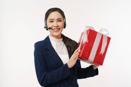 Téléchargez les photos : Jeune centre d'appels d'affaires portant un casque tout en tenant cadeau boîte cadeau souriant à regarder la caméra - en image libre de droit