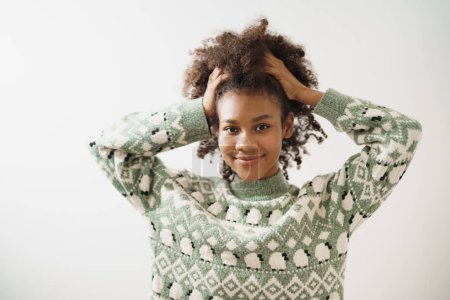 Téléchargez les photos : Portrait de belle afro-américaine attachée ses cheveux avec les deux mains levez-vous, souriant détente confortable isoler avec fond blanc et copier l'espace. - en image libre de droit