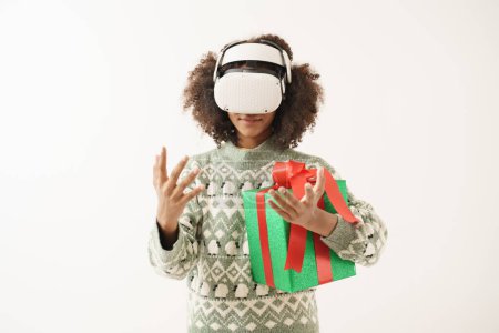 Téléchargez les photos : Jeune femme afro-américaine portant VR ou masque de réalité virtuelle avec boîte cadeau dans son bras. - en image libre de droit