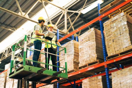 Téléchargez les photos : Travailleurs industriels et logistiques de l'entrepôt vérifiant les stocks sur l'élévateur de grue sur l'étagère de stock. - en image libre de droit