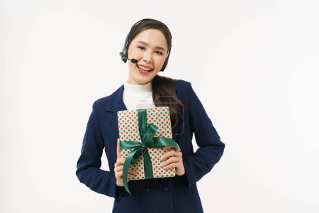 Téléchargez les photos : Jeune centre d'appels d'affaires portant un casque tout en tenant cadeau boîte cadeau souriant elle regarde la caméra. - en image libre de droit