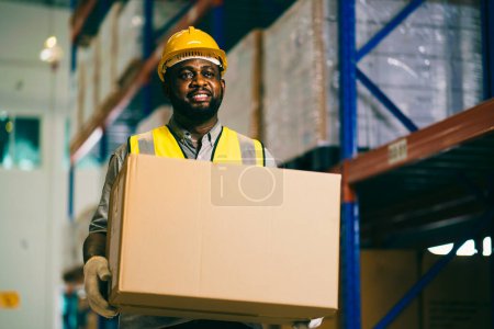 Téléchargez les photos : Travailleur dans un entrepôt tenant boîte en carton tout en regardant la caméra et souriant. - en image libre de droit