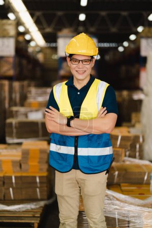 Foto de Retrato de un trabajador de ingeniería industrial asiático que usa sombrero blanco sonriendo profesionalmente en un fondo de fábrica de almacén, control de calidad, verificación de seguridad, ocupación profesional. - Imagen libre de derechos