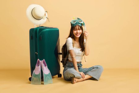 Foto de Feliz mujer joven asiática sonriendo y sentada en el suelo con el equipaje cerca con cosas divertidas para viajar. - Imagen libre de derechos