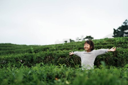 Téléchargez les photos : Enfant souriant profitant de l'air frais dans une plantation luxuriante d'arbres à thé. - en image libre de droit