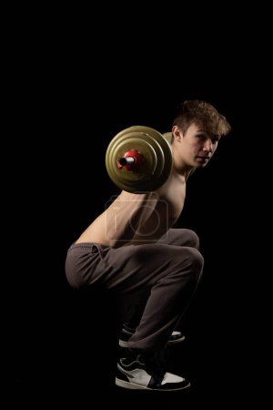Photo for A 17 year old shirtless muscular teenage boy holding a barbell across his shoulders to do squats - Royalty Free Image