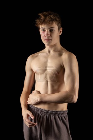 Téléchargez les photos : A portrait of a 17 year old shirtless muscular teenage boy against  a black background - en image libre de droit