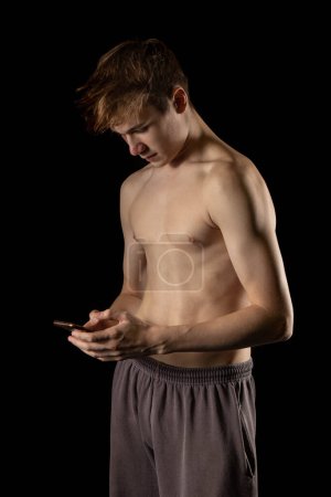 Photo for A 17 year old shirtless muscular teenage boy holding a mobil phone - Royalty Free Image