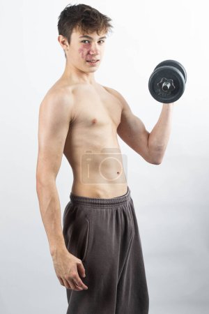Photo for A 17 year old shirtless muscular teenage boy exercising with a dumbbell - Royalty Free Image