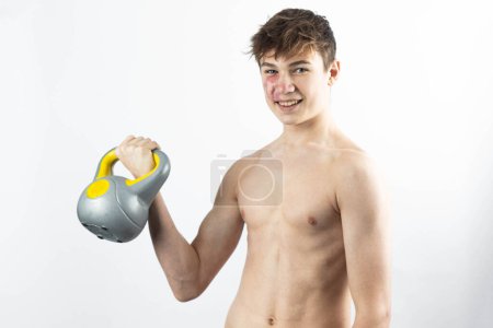 Photo for A 17 year old shirtless muscular teenage boy exercising his arms with a kettlebell - Royalty Free Image
