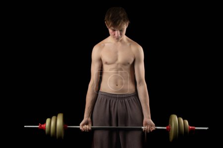 Photo for A 17 year old shirtless muscular teenage boy lifting a barbell against a black background - Royalty Free Image