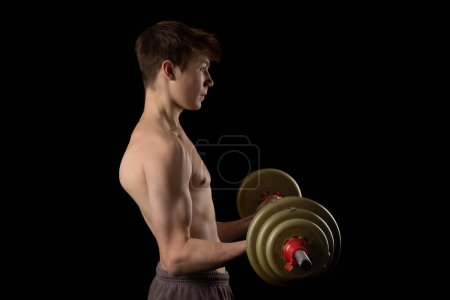 Photo for A 17 year old shirtless muscular teenage boy lifting a barbell against a black background - Royalty Free Image