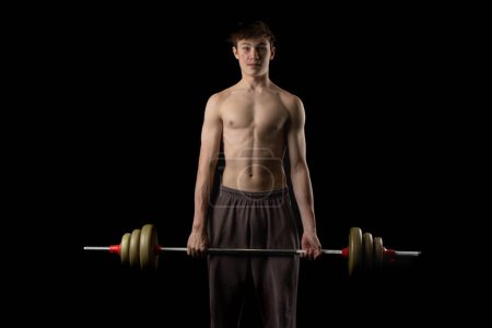 Photo for A 17 year old shirtless muscular teenage boy using a barbell against a black background - Royalty Free Image