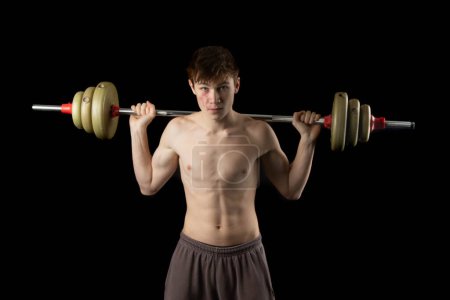 Photo for A 17 year old shirtless muscular teenage boy holding a barbell across his shoulders to do squats - Royalty Free Image