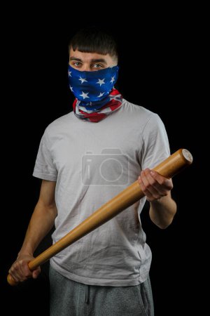 Foto de Adolescente con una máscara de bandera americana sosteniendo una bata de béisbol de una manera amenazante contra un fondo negro - Imagen libre de derechos