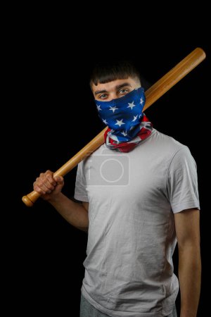 Foto de Adolescente con una máscara de bandera americana sosteniendo una bata de béisbol de una manera amenazante contra un fondo negro - Imagen libre de derechos