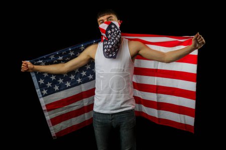 Foto de Adolescente en un chaleco blanco con una máscara de bandera americana y bandera sobre un fondo negro - Imagen libre de derechos