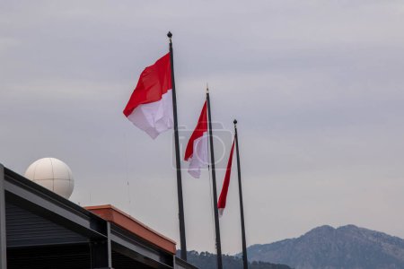 Foto de La Condamine, Mónaco, 22 de abril de 2023: - La bandera de Mónaco ondeando sobre Port Hércules, el principal puerto de Mónaco, ubicado en el barrio de La Condamine. - Imagen libre de derechos