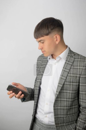 Foto de Joven emprendedor con chaqueta de traje y camisa de cuello abierto sin corbata leyendo un mensaje en su teléfono - Imagen libre de derechos