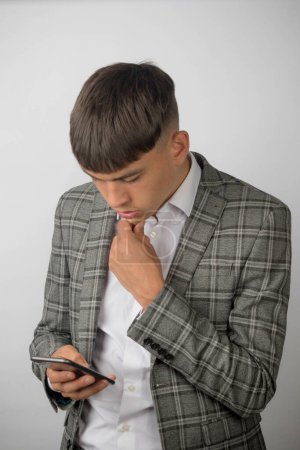 Foto de Joven emprendedor con chaqueta de traje y camisa de cuello abierto sin corbata leyendo un mensaje en su teléfono - Imagen libre de derechos
