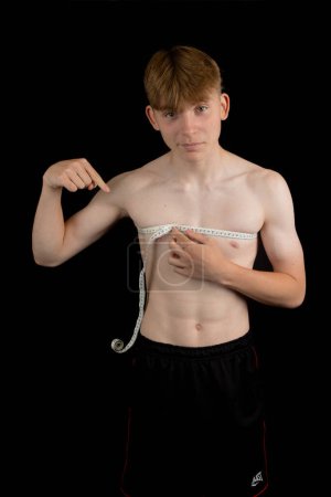 Photo for Portrait of a sporty shirtless teenage boy measuring his chest - Royalty Free Image