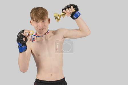Photo for Shirtless male teenage MMA fighter with a ttrophy and medal flexing his his muscles - Royalty Free Image
