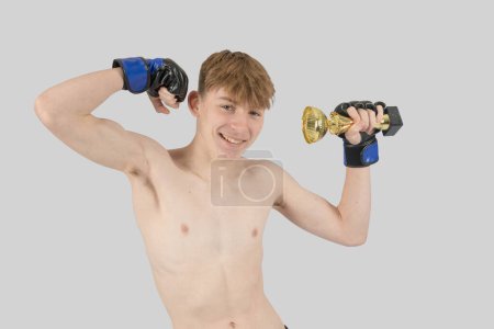 Photo for Shirtless male teenage MMA fighter with a ttrophy flexing his his muscles - Royalty Free Image