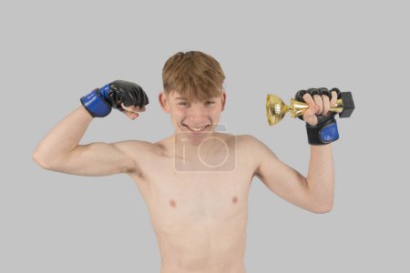 Photo for Shirtless male teenage MMA fighter with a ttrophy flexing his his muscles - Royalty Free Image