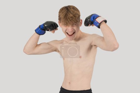 Photo for Shirtless male teenage MMA fighter flexing his arm mucles while yelling - Royalty Free Image