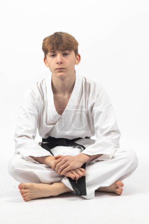 Ein 15-jähriger Karate Blackbelt Junge, der A Gi im Schneidersitz trägt