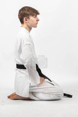 Ein 15-jähriger Karate Blackbelt Junge, trägt A Gi kniend in Seiza