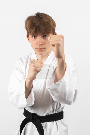 Ein 15-jähriger Karate-Schwarzgürtel-Junge trägt ein Gi mit erhobenem Arm