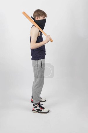 A Teenage Male Gang Member in a mask holding a baseball bat sideways