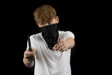 Un agresseur masculin adolescent contre un fond noir tenant un couteau