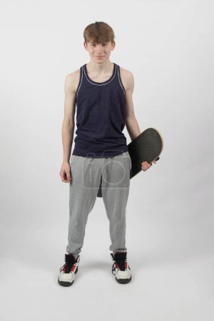 A fifteen year old skater boy holding a skateboard against a white background