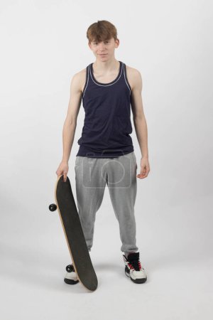 Ein fünfzehnjähriger Skaterboy mit einem Skateboard vor weißem Hintergrund