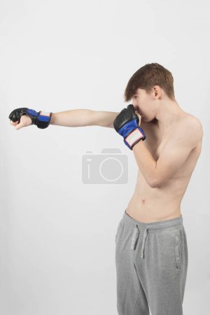 Ein hemdloser 15-jähriger männlicher Teenager-Boxer vor einem schlichten Hintergrund schlägt zu