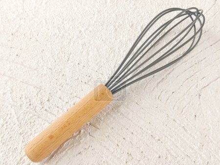 silicone whisk with wooden handle on white table. 