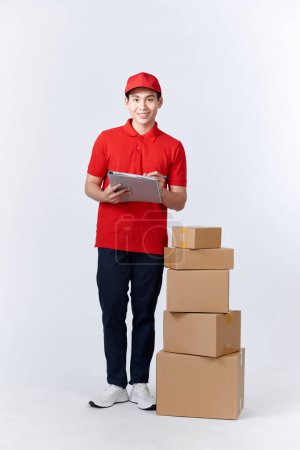 Photo for Confident deliveryman. Cheerful young deliveryman holding a cardboard boxes while standing in front of the box stack - Royalty Free Image