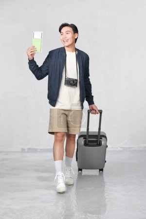 Foto de Happy young Asian tourist man holding passport with baggage going to travel on holidays - Imagen libre de derechos