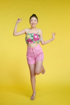 Foto de Hermosa mujer joven en camisa de flores y pantalones cortos de color rosa posando sobre fondo amarillo - Imagen libre de derechos
