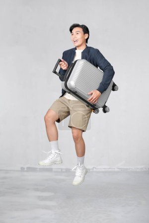 Foto de Jumping portrait of young fit healthy smiling handsome Asian tourist man with baggage ready to fly - Imagen libre de derechos