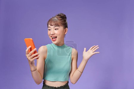 Téléchargez les photos : Heureuse femme asiatique sentiment de bonheur et debout tenir smartphone sur fond violet - en image libre de droit