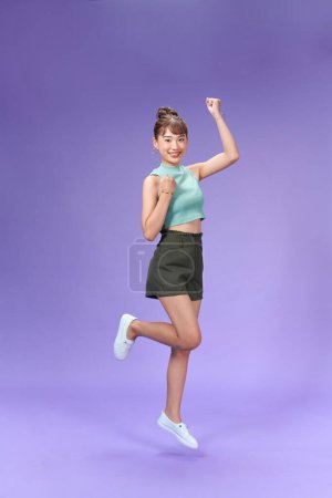 Photo for Full length portrait of a joyful young woman jumping and celebrating over purple background - Royalty Free Image